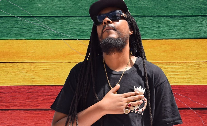 Don Dada holding left hand to chest reggae colours background Don Dada holding left hand to chest reggae colours background